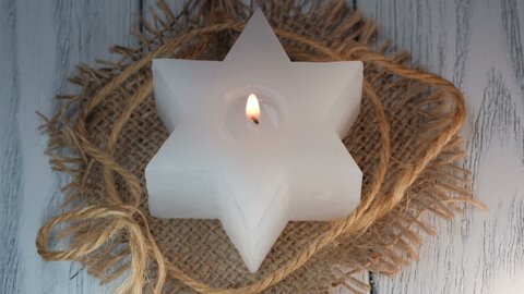 White candle in the shape of a six-pointed star burns on a burlap lining close-up 4k resolution