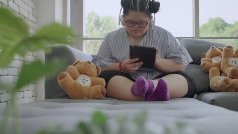 young Asian girl with Down's syndrome is playing a tablet alone in the room
