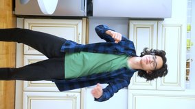 vertical video. handsome curly guy dancer cheerfully dancing at home in the kitchen .