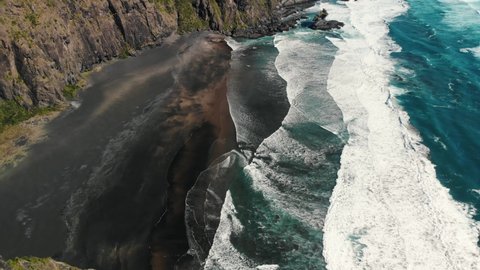 aerial footage waves crash on the beach ocean clear water and rocky cliff in a natural paradise, new zeland Karekare