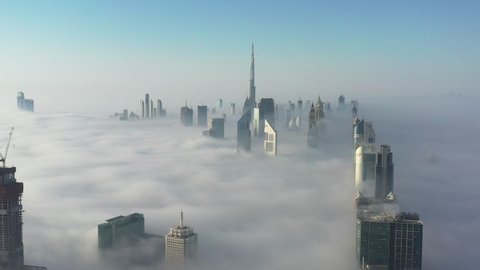 Aerial birds eye view of Dubai city urban futuristic skyline during fog; World's tallest building and high rise skyscrapers covered in dense fog in Dubai winter season