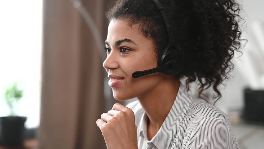 Side view of an African-American female support officer wearing a headset takes a call, a smiling call center employee helps to customer online, close-up view Royalty-Free Stock Footage #1067036935