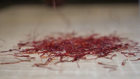 Poetic closeup of dried crimson shaffron pestles flying and falling on a kitchen table in slow motion.It looks inspiring, cheerful and high-art.