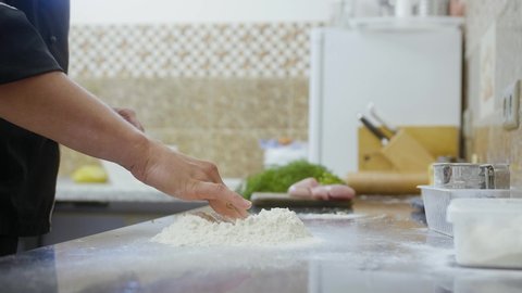 Men is making a deep in the flour before preparing a dough.  Cracking an egg into dough. Food preparing and bakery process.  closeup