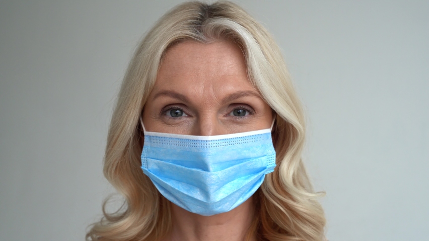 Smiling 50s middle aged woman taking off medical face mask looking at camera. Mature lady removing facemask feeling happy after covid quarantine concept. Close up view portrait Royalty-Free Stock Footage #1067038978