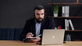 Handsome bearded man studying online using laptop web camera, writing lecture in notebook.Online education, remote working, home education.Online meeting, video call, video conference, courses online.