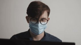 student teenager in medical a protective mask studying video call remotely at home. coronavirus stay home distance learning concept. young worker man in protective mask works at laptop in office