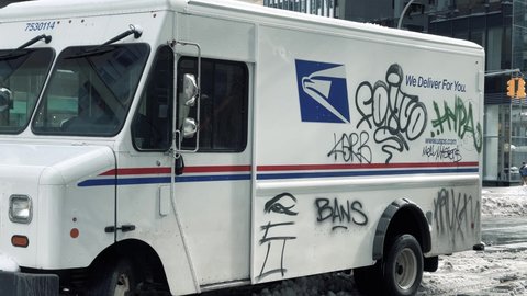 NYC, USA - FEB 3, 2021: USPS delivery truck littered with graffiti tags - snow on street in New York City.