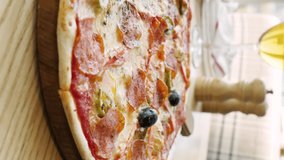 baked pizza with sausage, vegetables and olives. oil is poured on pizza close-up