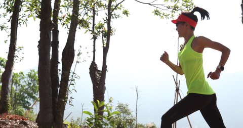 Fitness woman trail runner running on sunrise tropical forest mountain peak, slow motion