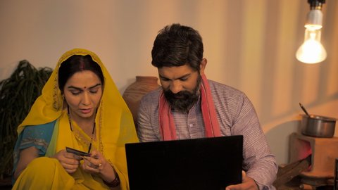 Indian village couple - Using the internet and doing online shopping. Rural couple using debit credit card to make an online payment from their home - modern Indian villagers