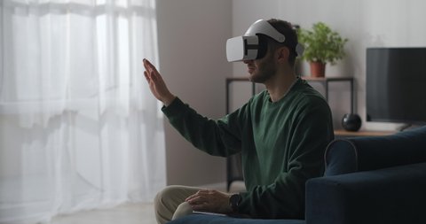 adult man with head-mounted display is viewing virtual screen and swiping by hand, vr technology