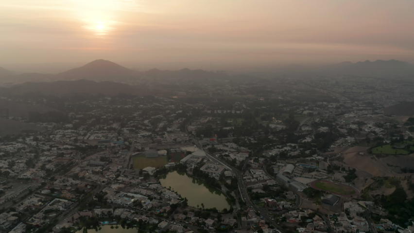 Aerial track shot of the sun setting over the city of Lima Peru, showing the golden haze over the city.