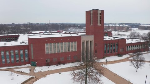 Front entrance, facade of large American school, college building during winter. Sidewalks are cleared of snow. Aerial drone shot.