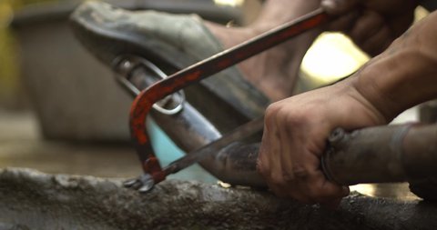 A man cutting bike silencer pipe with hacksaw.
