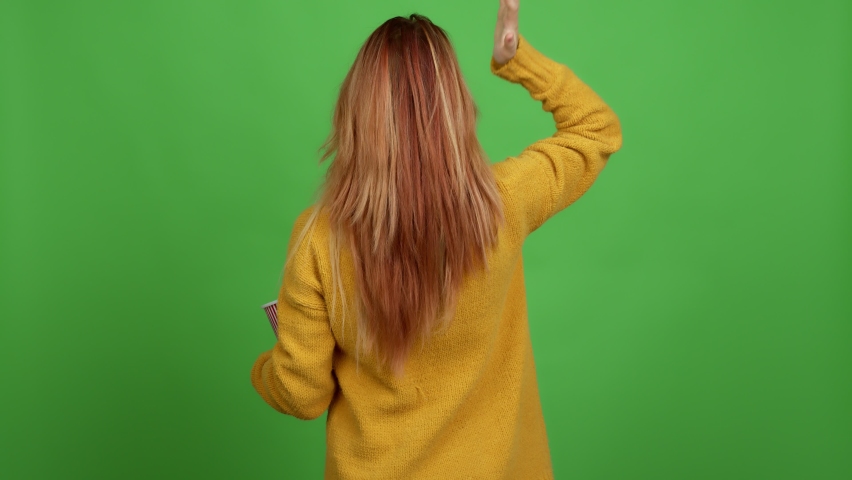 Teenager girl holding a bowl of popcorns on back position looking back while scratching head over isolated background