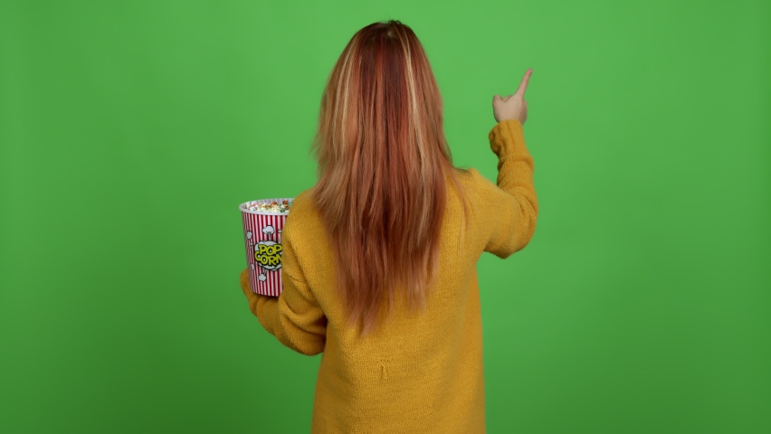 Teenager girl holding a bowl of popcorns pointing back with the index finger over isolated background
