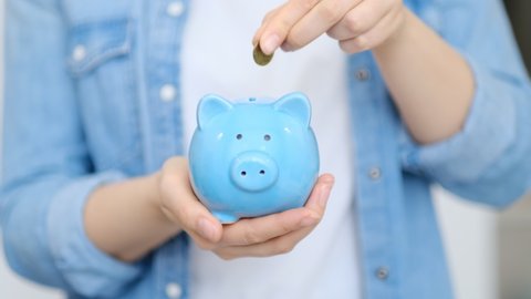 Savings concept. Woman holding piggy bank and coins on light background. Woman putting coin into piggy bank. close up view. Slow motion video. High quality 4k stock footage.
