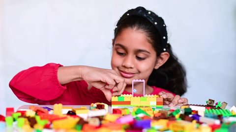 4k video of a cute little Indian girl playing with colourful toy building blocks and having fun.