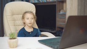 A 6-year-old girl wearing a medical mask makes a video call on a laptop
