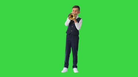Little boy in a bow tie playing the trumpet and looking at camera on a Green Screen, Chroma Key.
