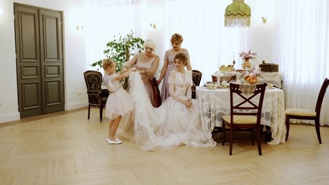 Women of different ages look at the bride's dress. They are happy and smiling. Retro style of the room.Senior woman, mid age woman, young girl and child