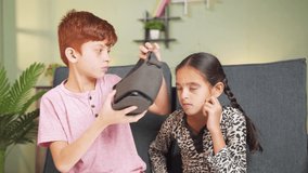 Young kid helping his sister to wear VR or virtual reality headset at home - concept of togetherness, bonding and use of technology