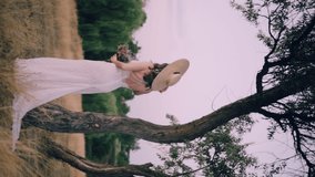 Portrait of a young bride. A woman in a wedding dress stands and looks at the camera in nature. Vertical video.
