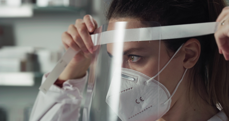 Cinematic macro shot of female pharmacist consultant putting on protective N95 respirator mask and visor in pharmacy. Concept:covid-19, protection, coronavirus, safety, health care and medical workers | Shutterstock HD Video #1067085406