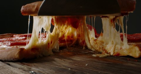 Close up shot of taking a piece of freshly baked pizza with tasty stretchy cheese. Delicious Italian pizza from the oven on black background. food and drink 4k footage