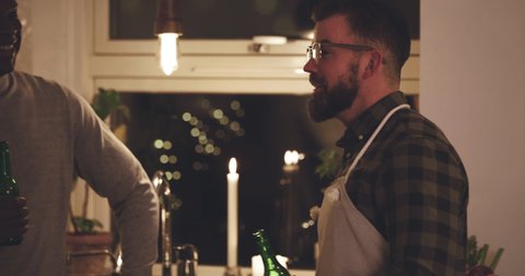 Two diverse young men laughing while talking together over beers in a kitchen during a dinner party
