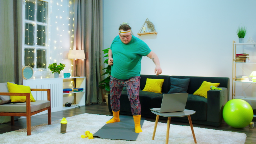 Funny fat guy in the living room using laptop to do a online course for karate he wearing a sport equipment Royalty-Free Stock Footage #1067087290