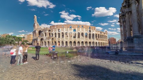 Many tourists visiting The Colosseum or Coliseum timelapse hyperlapse, also known as the Flavian Amphitheatre in Rome, Italy. Green lawn. Blue sky with clouds at sunny day