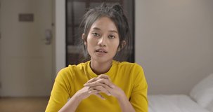 POV of young beautiful asian woman talk and looking to camera. Pretty girl work or study online at home. Lady in yellow casual clothes at house during quarantine. Social distance new normal concept.