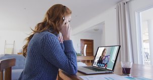Caucasian woman using laptop and phone headset on video call with female colleague. Staying at home in self isolation during quarantine lockdown.