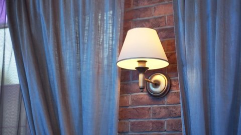 Wall light on red brick wall near gray curtains in apartment