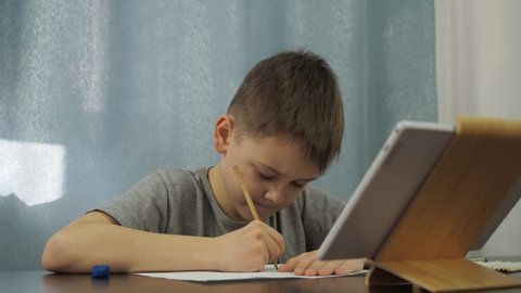 a boy in a gray T-shirt draws a picture with a pencil from a tablet. art lessons online.