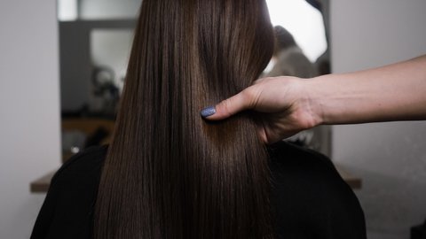 Demonstration of smooth and silky brunette hair after straightening it with a steampod. The master shows a lock of smooth, shiny and silky brunette hair after straightening it with a steampod. 4K