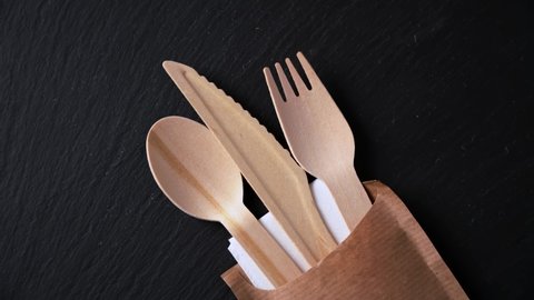 Disposable biodegradable tableware made of wood spoon, knife and fork on marble texture. Close-up.