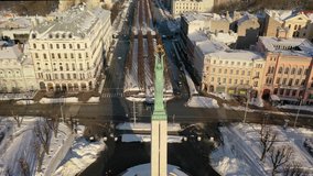 Riga, Latvia, Baltics. Beautiful panoramic aerial 4K video from flying drone to Freedom Square with the Latvia Freedom Monument on a snowy, sunny winter day.