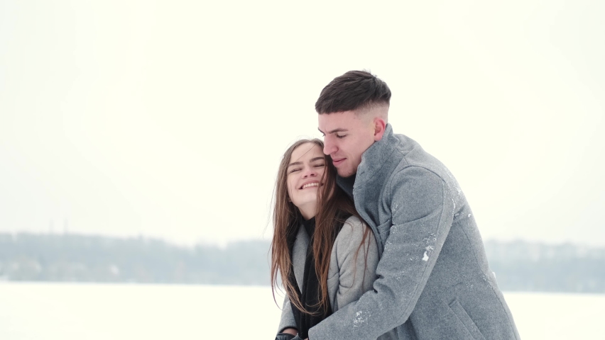 Romantic young couple wrapped in blanket standing together at winter landscape.