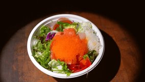 This video shows chop sticks taking bites of food from a top view angle out of a carry out sushi salad bowl.