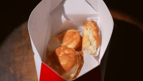 This close up video shows anonymous hands grabbing a fresh biscuit from a carry out container.