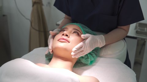 Beauty clinic doctor or nurse and carefully touch a customer woman face who lie on bed and cover hair. Business concept of beauty clinic service for beauty of skin and body. Footage B roll 4k.