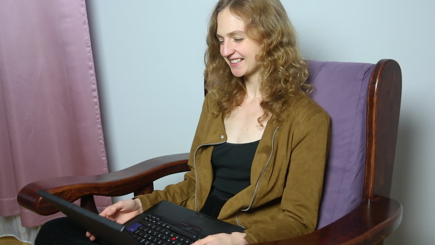 Young cheerful woman doing video call on laptop while working at home