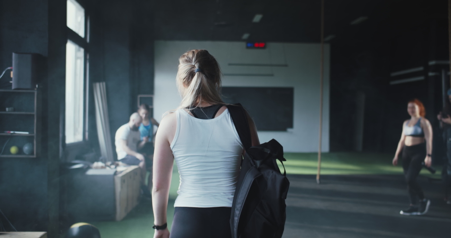 Lifestyle fitness community club. Camera follows young sporty blonde woman enter modern gym, high-fiving happy friends. Royalty-Free Stock Footage #1067124193