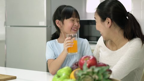 Asian family drink orange juice in kitchen room at home. Pregnant woman and daughter making orange juice smoothie at home. Family making healthy drinks while being quarantine at home.