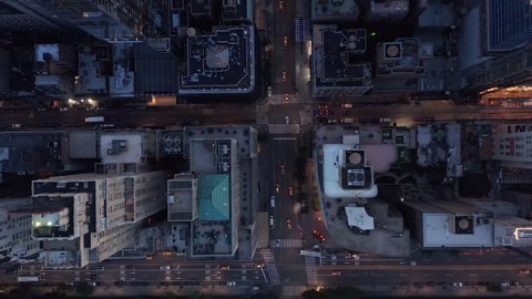 Slow Aerial Drone View of City Street with Skyscraper Rooftops and Road traffic, Birds Eye Overhead Top Down View at Dusk or Night with flashing City lights