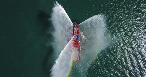 A floating modern ship sprays jets of water, demonstrates fire fighting water cannon, sprays water as firefighter boat top view from the drone