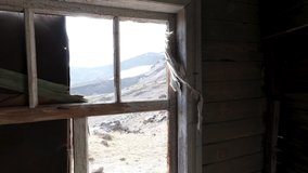 View through the windows inside a wooden abandoned house. Clip. Old ruined wooden building and a hill slope outside.